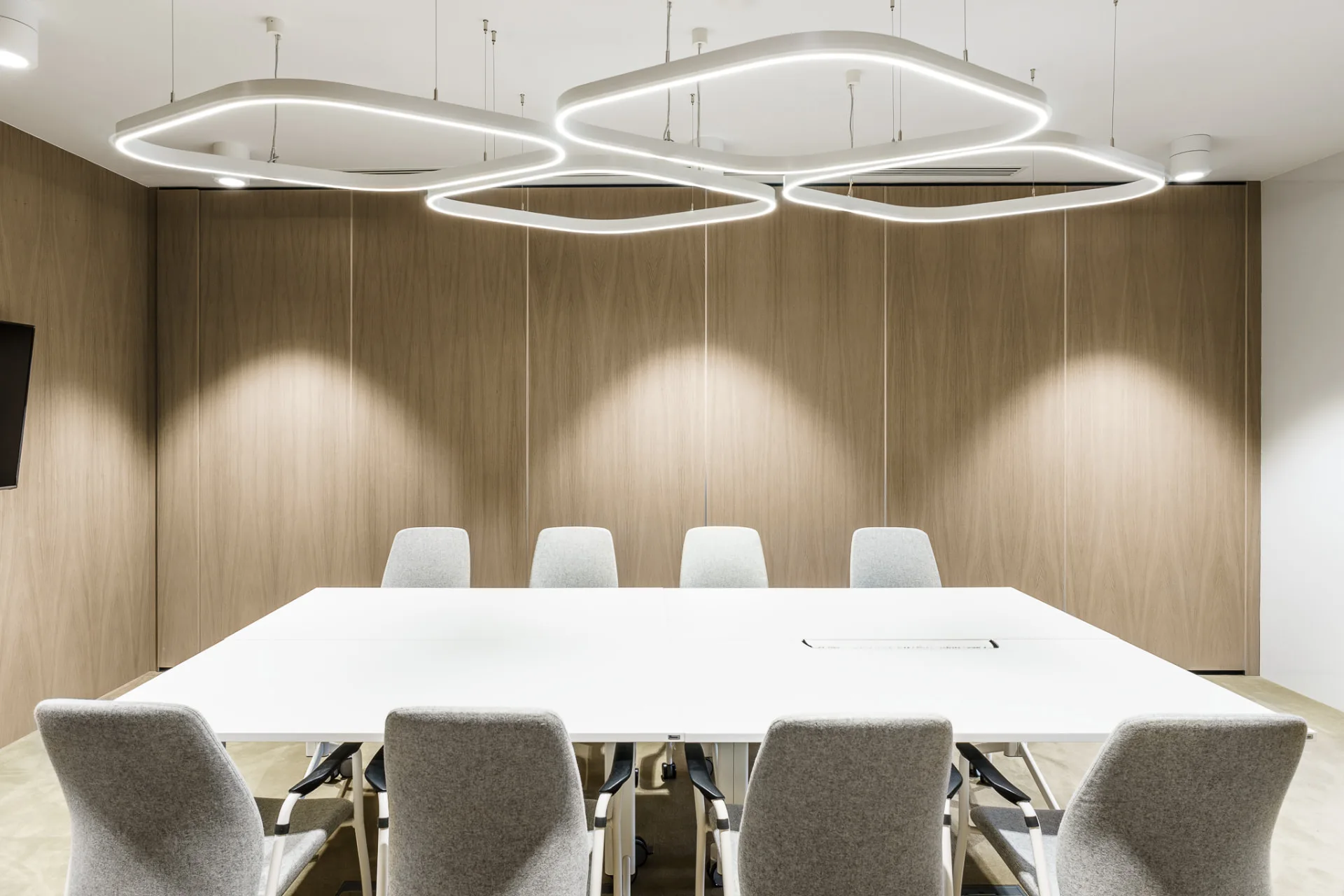 Meeting room with suspended ring luminaires and downlights washing a timber wall with soft pools of light